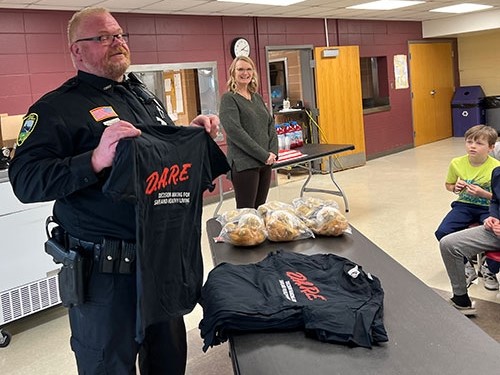D.A.R.E. to wear ... Lansing/New Albin Police Chief Conrad Rosendahl displays one of the t-shirts that were given to fifth and sixth grade students in the Eastern Allamakee Community School District (EACSD) who participated in the inaugural year of the local Drug Abuse Resistance Education (D.A.R.E.) program this past school year. Pictured in the photo background is EACSD fifth grade teacher Lisa Welsh, who was instrumental in facilitating the program for her students